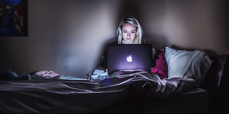 una mujer sentada en la cama en la oscuridad con una computadora portátil